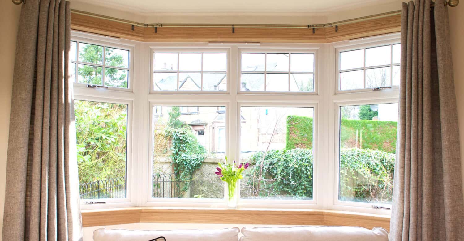 Living room with large bay window. White casement windows with royal oak sills and surrounds. Cream sofa and cushions.