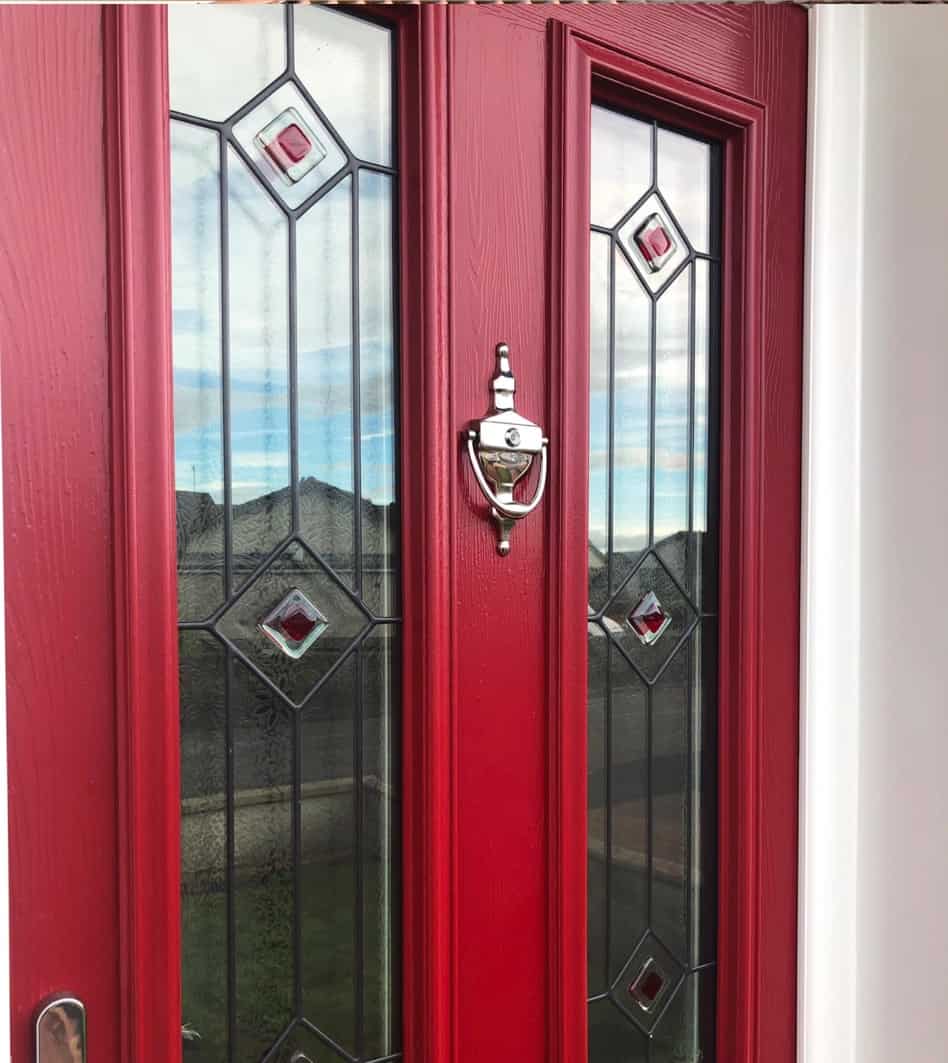 Close up of a red engineered timber front door. Decorative glazed panels and urn door knocker