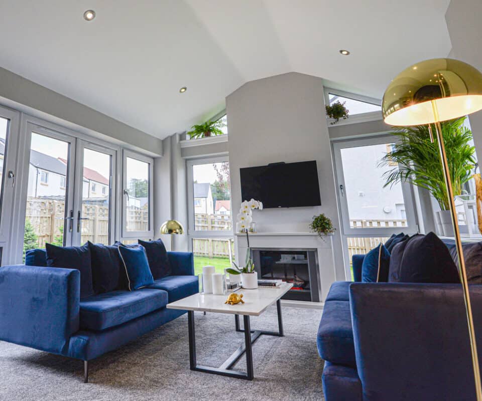 Internal view of open plan sunroom with french doors and blue velvet sofas