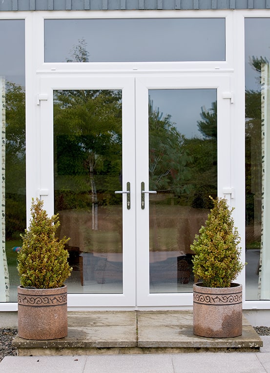 Close up of white french doors with fan light and two potted trees