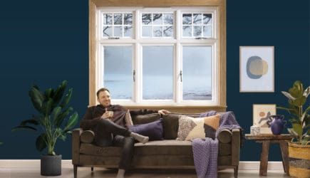 Man sitting on the sofa in a blue living room with a white casement window