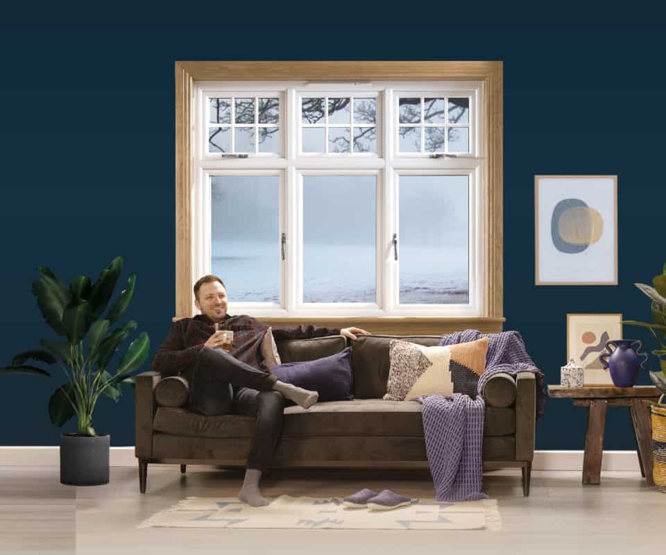 Man sitting on the sofa in a blue living room with a white casement window