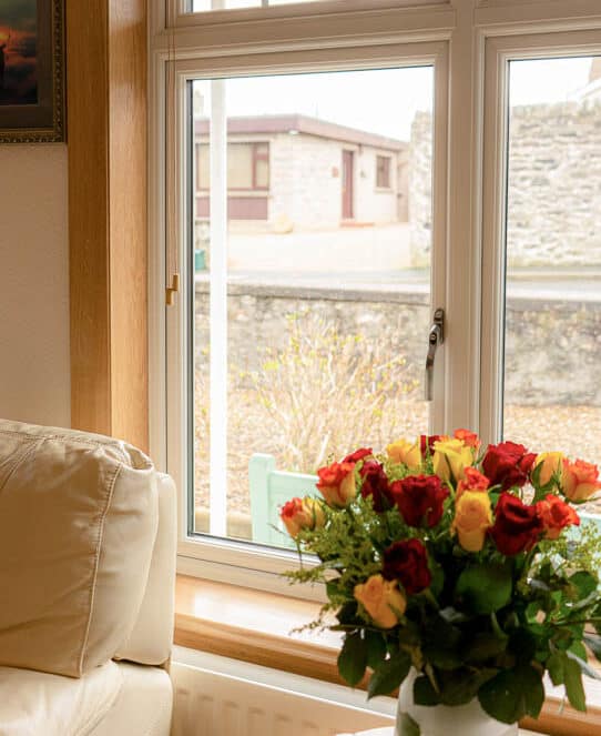 Close up of white casement window and a vase of red and yellow roses