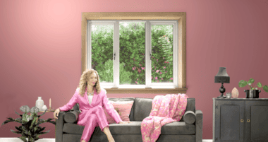 Woman dressed in a pink suit sitting on a sofa in front of a white casement window