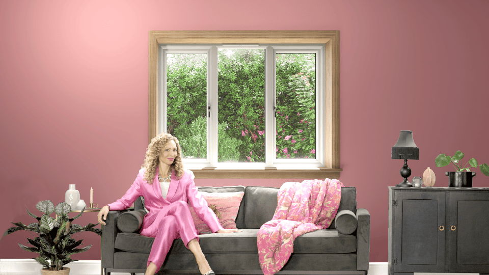 Woman dressed in a pink suit sitting on a sofa in front of a white casement window