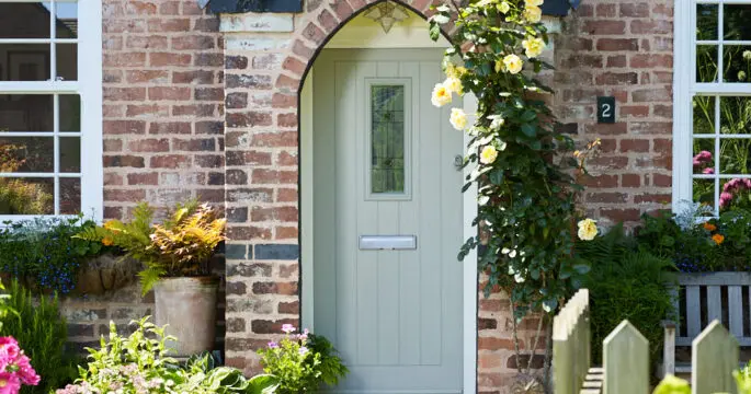 A duck egg blue TimberLuxe engineered timber door with a central, decorative glass pane, complete with a stainless steel letterbox. The door is positioned within a brick alcove.