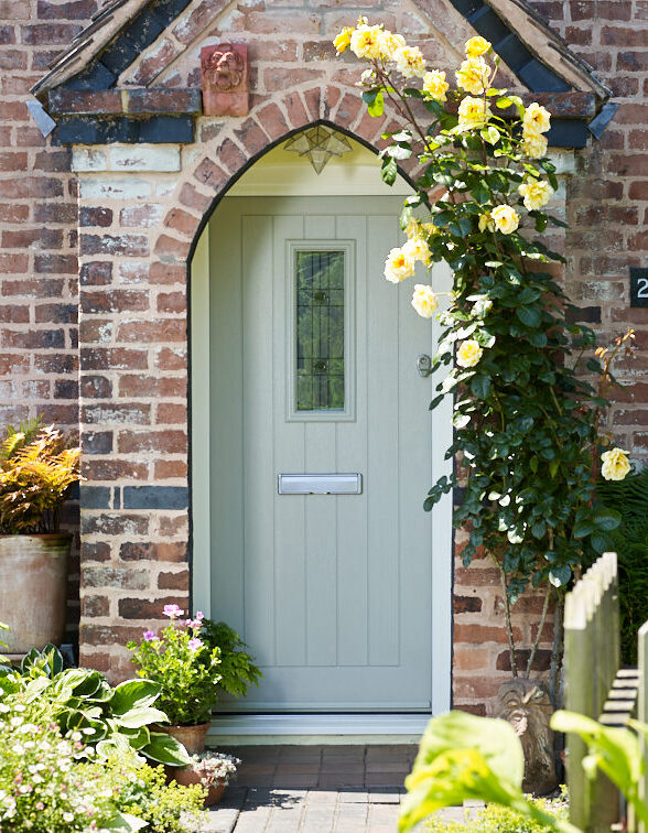 A duck egg blue TimberLuxe engineered timber door with a central, decorative glass pane, complete with a stainless steel letterbox. The door is positioned within a brick alcove.