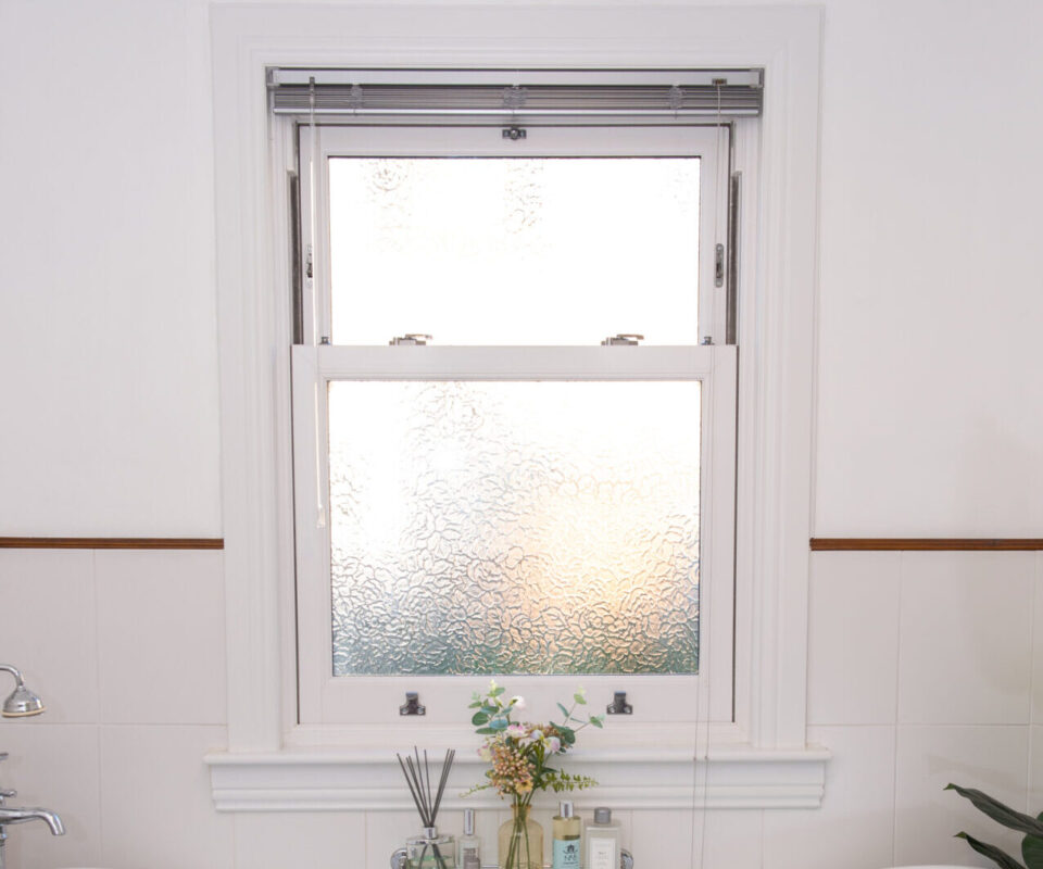 Lorimer uPVC sliding sash window complete with white sills and surrounds, located in a bathroom, positioned above a white free standing bath