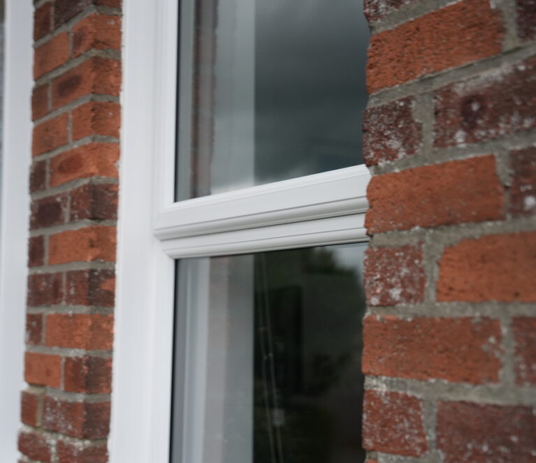 close up of white uPVC Lorimer casement window. Contrasting against red brickwork
