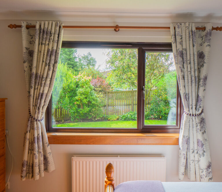 Interior view of a rosewood Lorimer casement window in a bedroom overlooking the garden in Doune