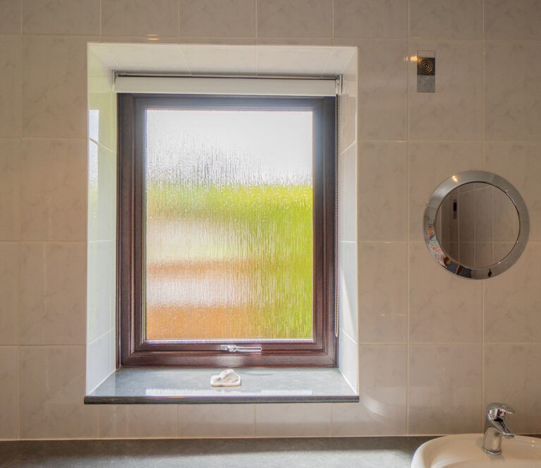 Interior view of a rosewood Lorimer casement window with frosted glass in a bathroom overlooking the garden in Doune
