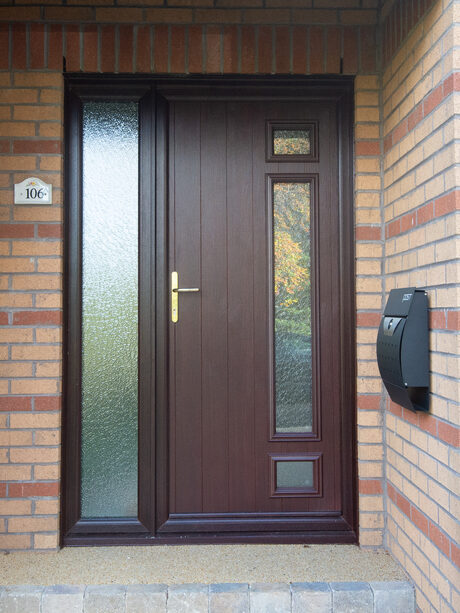 Exterior shot of a Rosewood coloured front door, complete with a frosted glass side screen on the left and gold lever handle.