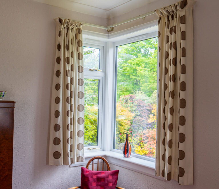 Internal view of a Lorimer casement window in Falkland, situated in the living room. The corner window is complete with gold handles and a painted white sill and surround.