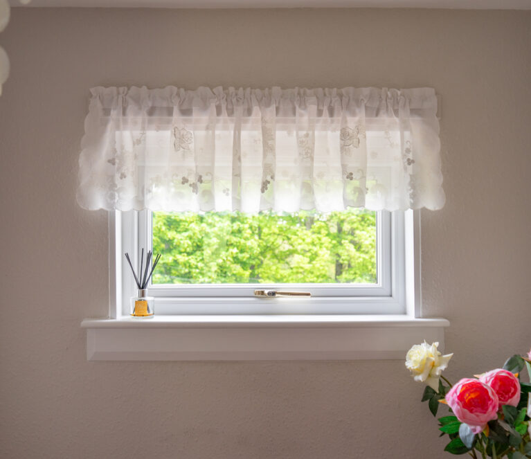 Internal view of a white lorimer casement window in Falkland home. Complete with a gold handle and net pelmet.